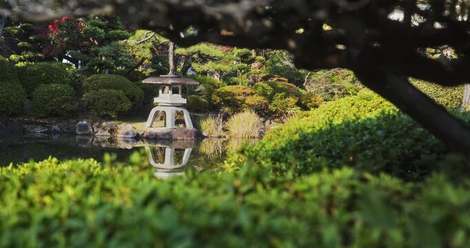 Medium tracking shot of old stone Japanese lantern on edge of pond