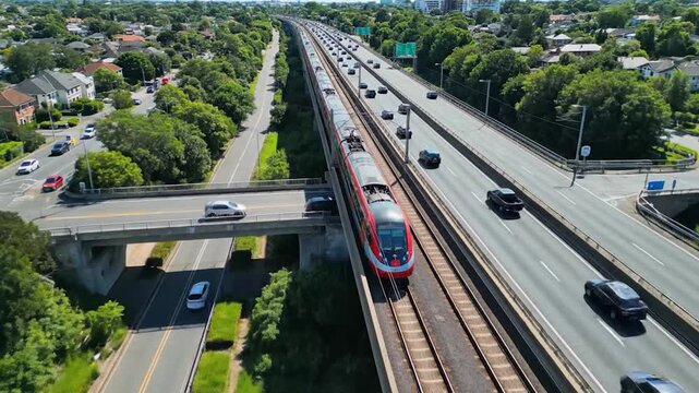 An aerial view captures a modern red train speeding alongside a busy highway