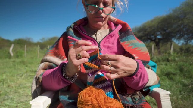 Mujer tejiendo a crochet con lana de colores al aire libre en entorno rural