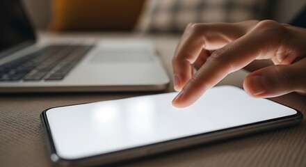 Person using a smartphone near an open laptop on a desk