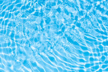 Obraz premium Blue water with ripples on the surface. Defocus blurred transparent blue colored clear calm water surface texture with splashes and bubbles. Water waves with shining pattern texture background.