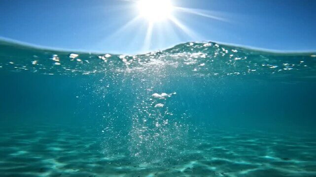 Sunlight shines through the clear ocean surface with bubbles rising from