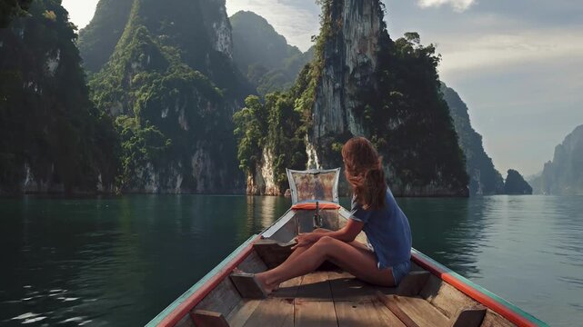 Lifestyle video of pretty travel woman sitting in wood long tail boat on tropical limestone cliffs . Dolphins family jumping from water.