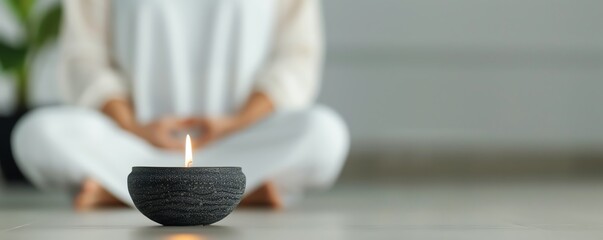 Lit candle in foreground with blurred person meditating behind, symbolizing mindfulness practice, relaxation, yoga routine, and mental wellness.