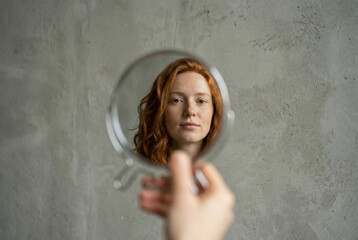 A woman's reflection in a round mirror against a gray wall 