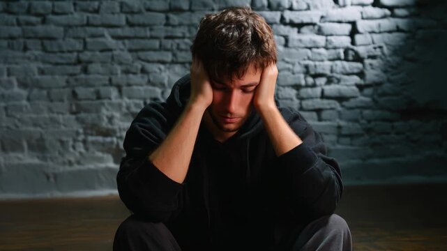 A Young Man Experiencing Deep Emotion and Isolation in a Dimly Lit Room, Reflecting Contemplation and Inner Turmoil While Seated Against a Brick Wall, Showcasing the Struggles of Mental Well-Being.