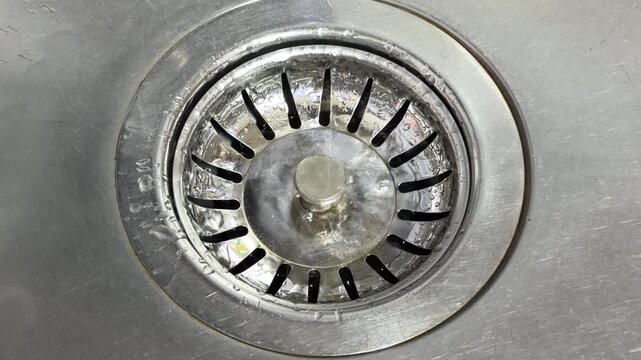 Individual water droplets fall from a faucet into a stainless steel basin. Each drop strikes the metallic surface, producing a clear, rhythmic ticking or plinking sound.