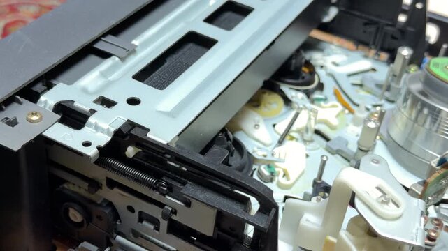 A vintage VCR mechanism lifts and ejects a VHS tape from the player. The internal gears and metal chassis produce a rhythmic mechanical clatter and a final metallic thud.