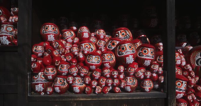 Slow motion dolly in on large pile of daruma dolls in wooden structure