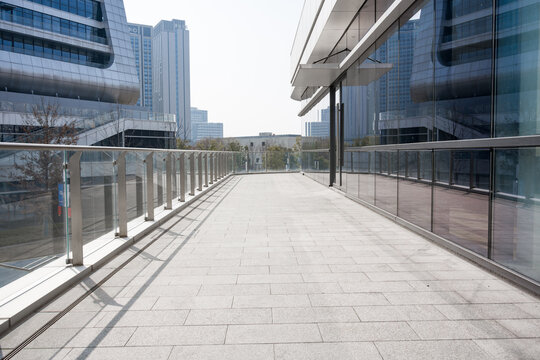 Empty modern urban skywalk corridor with glass railings and geometric paving under clear daylight