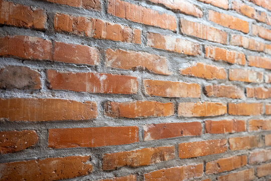 Close up of red brick wall with visible mortar joints and rough masonry texture, angled perspective construction background.