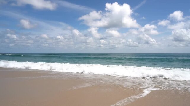 View of waves crashing on the shore with clouds above and a beautiful blue sky