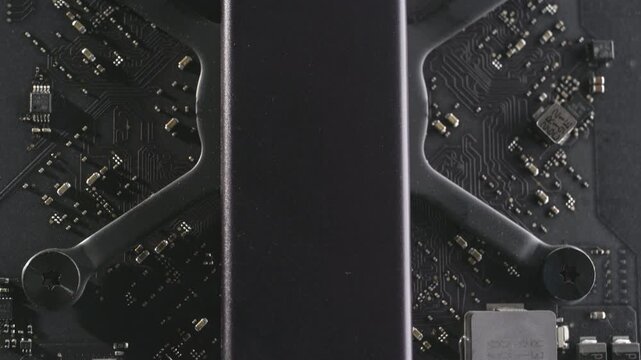 Macro shot inside a dark aluminium computer, highlighting SSD solid-state drive, motherboard, capacitors and components. Dramatic lighting, metallic, matten modern, reflective interior hardware.