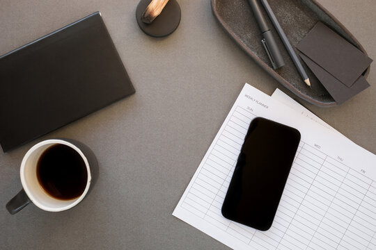 Elegant flat lay of a dark office desk featuring smartphone mockup, a paper organizer, black stationery, coffee and palo santo.