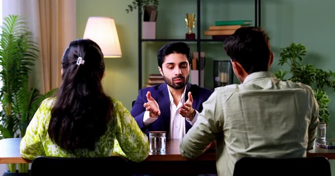 Indian couple visiting discussing with officer or executive shaking hands sitting across table after successful financial consultation and investment deal closure in modern corporate office interior