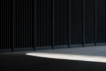 Dark vertical striped wall with contrasting light and shadow on concrete ground