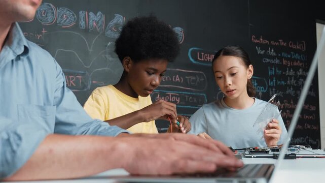Young student fixing controller while teacher programming engineering code at STEM class. Closeup of instructor hand typing computer while smart girl using electronic tool and blackboard. Edification