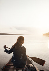 Fototapeta premium Canoeing, reflection and woman on lake for holiday, explore or adventure with back view in nature. Boat, think or person with paddle for summer vacation, travel or sunshine with mockup space by water