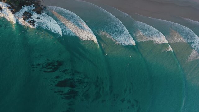 Rolling ocean waves form parallel lines as turquoise water meets a quiet sandy beach