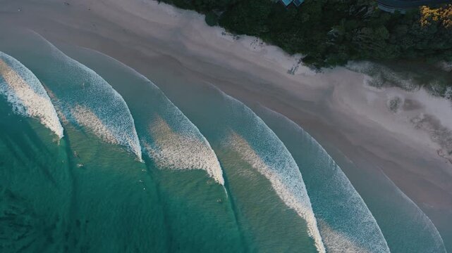 Broad wave fronts roll in sequence across clear water beside an undeveloped beach