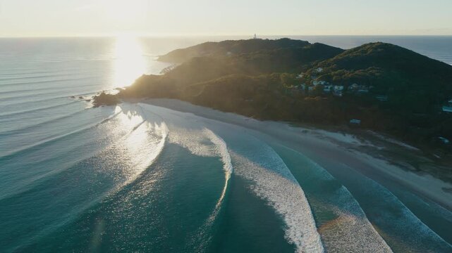 Evening light washes the coast as long waves approach a quiet sandy shoreline