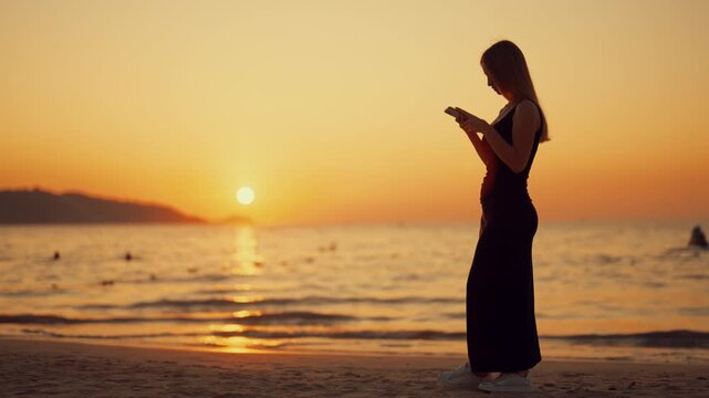 Romantic atmosphere on ocean beach, beautiful woman with mobile phone in hands. Lonely lady using smartphone for communication in social media, internet addiction and gadgets overuse, summer vacation