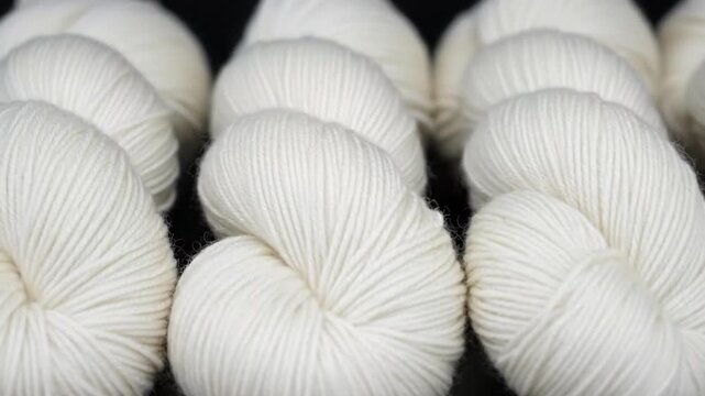 Row of neatly arranged white spherical yarn skeins on black surface capturing texture and precision for craft and textile industry