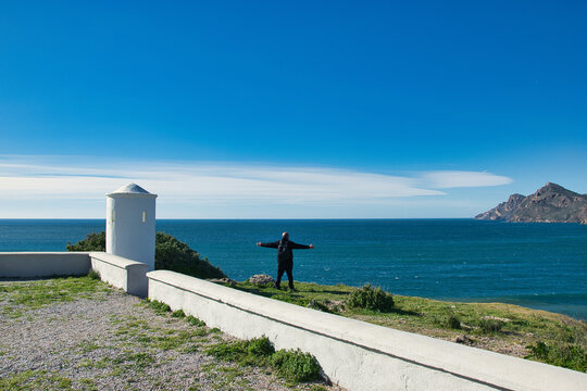 Man in black with his arms outstretched towards the sea