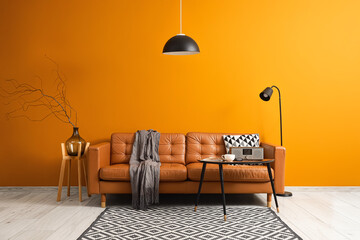 Obraz na płótnie Canvas Interior of stylish living room with brown sofa, coffee table and standard lamp near orange wall