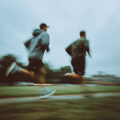 Two athletic men run fast outdoors with motion blur under overcast sky