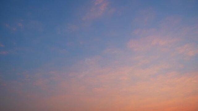 Sunset sky timelapse video with layered altocumulus and stratocumulus clouds glowing in warm orange and soft pink hues, gradually fading into deep blue twilight, highlighting dynamic cloud textures.

