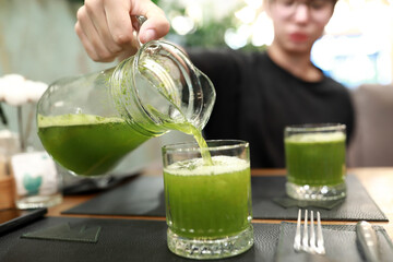 Man pouring green vegetable juice from pitcher into glass