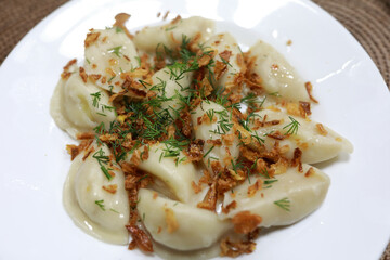 Plate of boiled dumplings with crispy fried onion and fresh dill