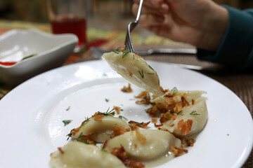 Woman lifting homemade dumpling with fork from white plate