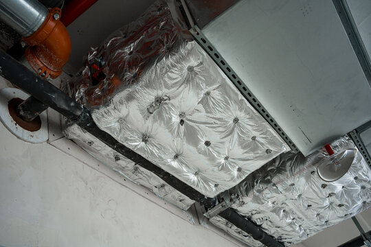Silver reflective insulation cotton wrapping ventilation ducts beneath ceiling in industrial setting