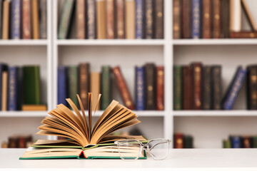 Open book and eyeglasses on table in stylish home library, closeup