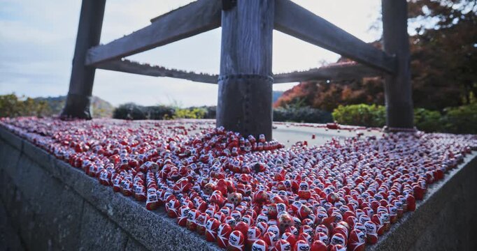 Hundreds of tiny daruma dolls on cement platform in Japan - wide, steady cam shot