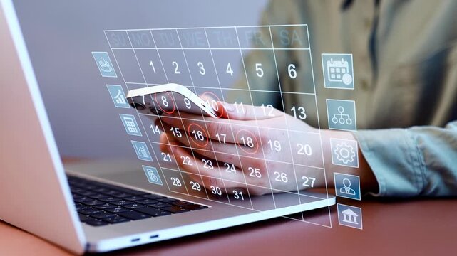 Person checks calendar on mobile phone while sitting at desk with laptop during daytime.