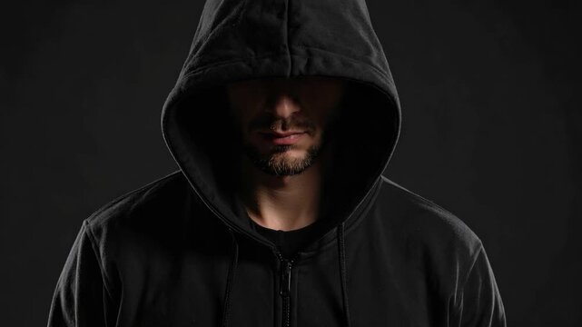 Anonymous man with beard wearing a black hoodie with hood up in dark studio setting