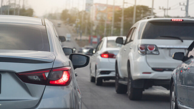 Rear side of luxury grey car with turn on brake light. Many cars parked in a queue on asphalt road. Background of roadside hill with light traffic and blurred of city and trees.