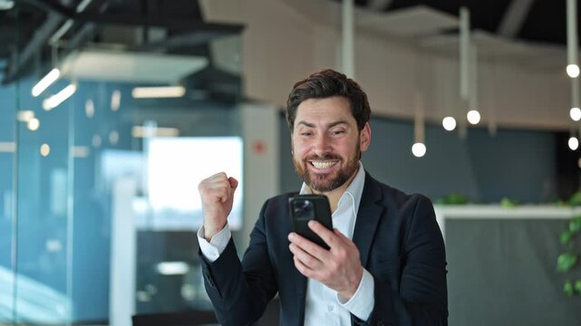 Executive in modern office discovers successful outcome on mobile device, demonstrating triumph and happiness with gesture.