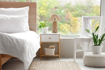 Interior of stylish bedroom with big window, houseplant and bedside table near cozy bed