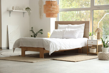 Interior of stylish bedroom with big window, houseplants and bedside table near cozy bed