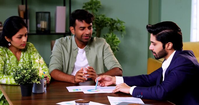 Indian couple meeting shaking hands with financial planner or ca in his office with laptop after reviewing growth reports and projections during serious investment discussion across table in office