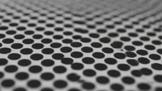 A close-up view of a repeating pattern of black ovals on a white surface with blur
