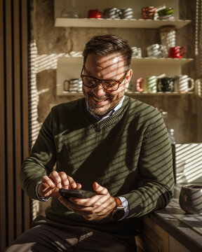 Man checking smart phone in kitchen during morning coffee routine