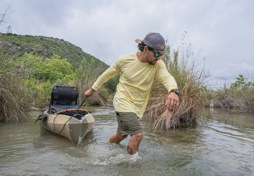 Hispanic Male Angler Pulling Fishing Kayak Through Shallow River