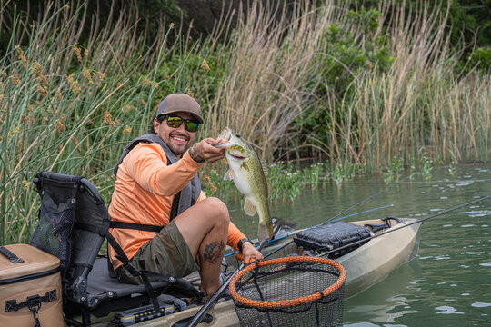 Hispanic Male Angler Displaying Bass Catch in Kayak on Lake
