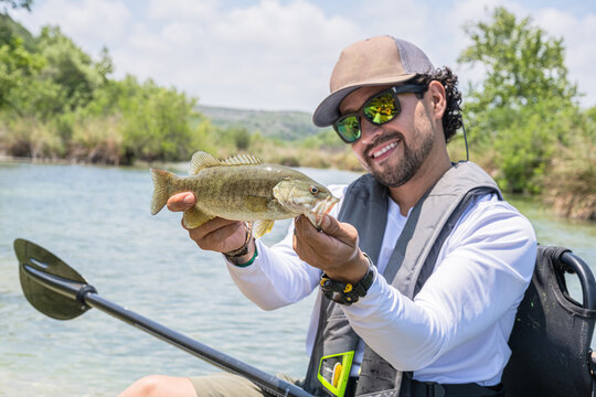 Hispanic Male Angler Proudly Displaying Bass Catch on River