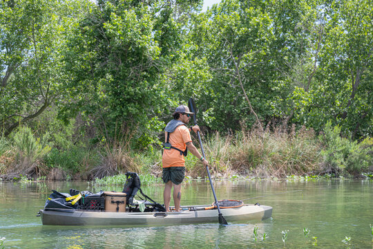 Hispanic Male Angler Standing and Paddling Fishing Kayak on River